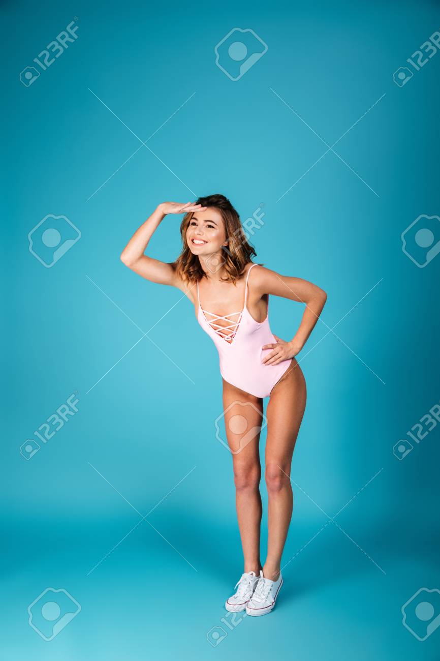 青い背景の上に孤立した遠くに立ち 遠くを見ながら水着ポーズを着た笑顔の少女の全長の肖像画 の写真素材 画像素材 Image