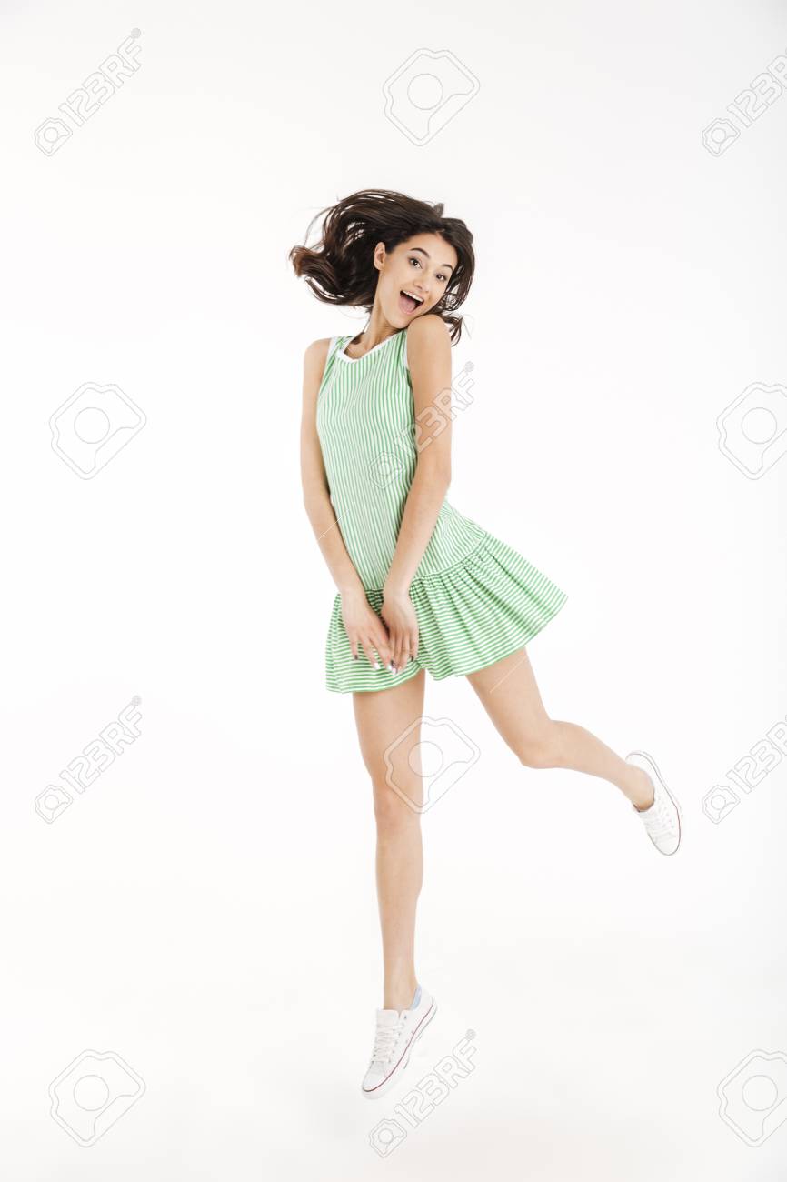 つま先にジャンプし 白い背景の上に隔離されたカメラを見ながらポーズを取るドレスを着た楽しい女の子の完全な長さの肖像画 の写真素材 画像素材 Image