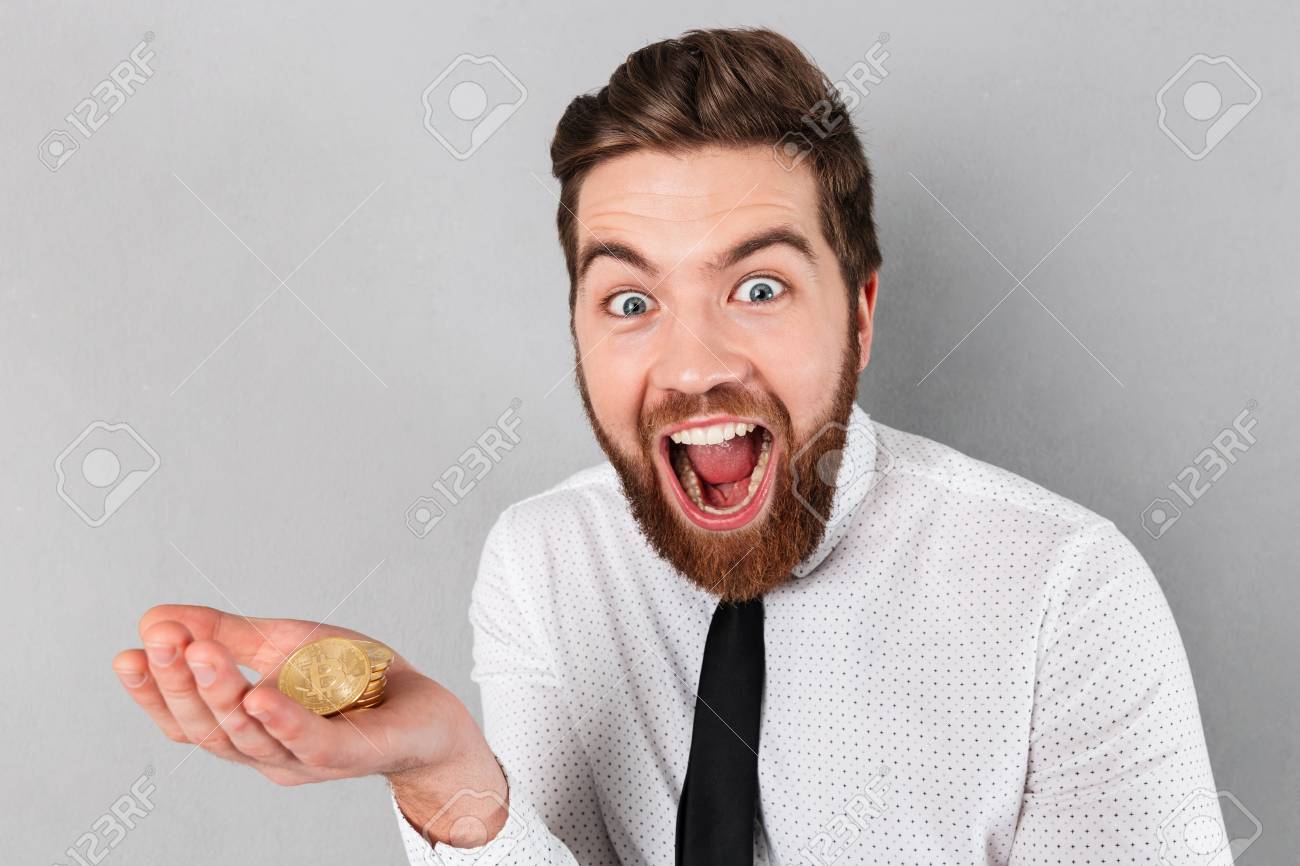 그의 팔에 황금 비트 코인을 보여주는 행복 한 사업가의 초상화는 회색 배경 위에 절연 로열티 무료 사진, 그림, 이미지 그리고  스톡포토그래피. Image 95862099