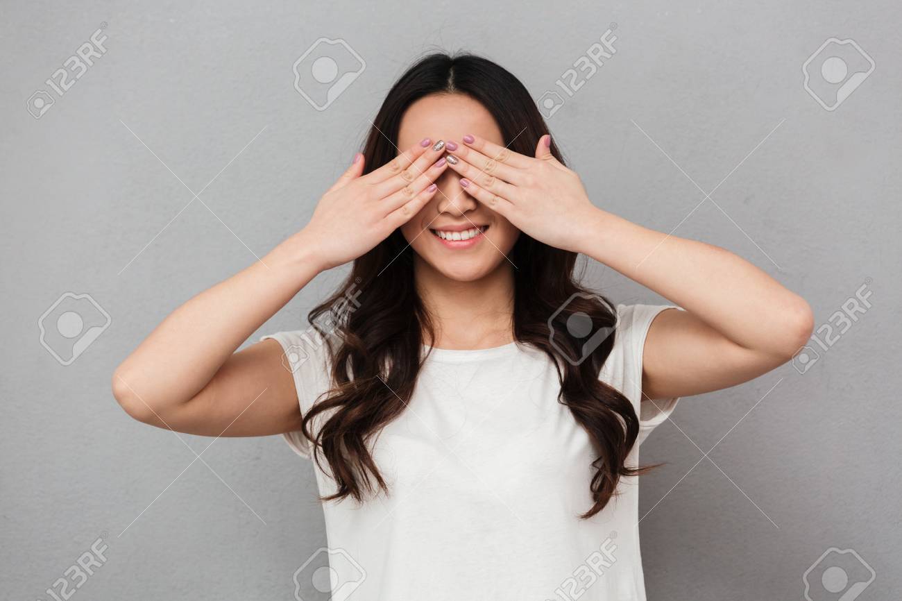 長い髪の笑顔と灰色の背景に隔離された手のひらで顔を覆う素敵なブルネットの女性の肖像画 の写真素材 画像素材 Image