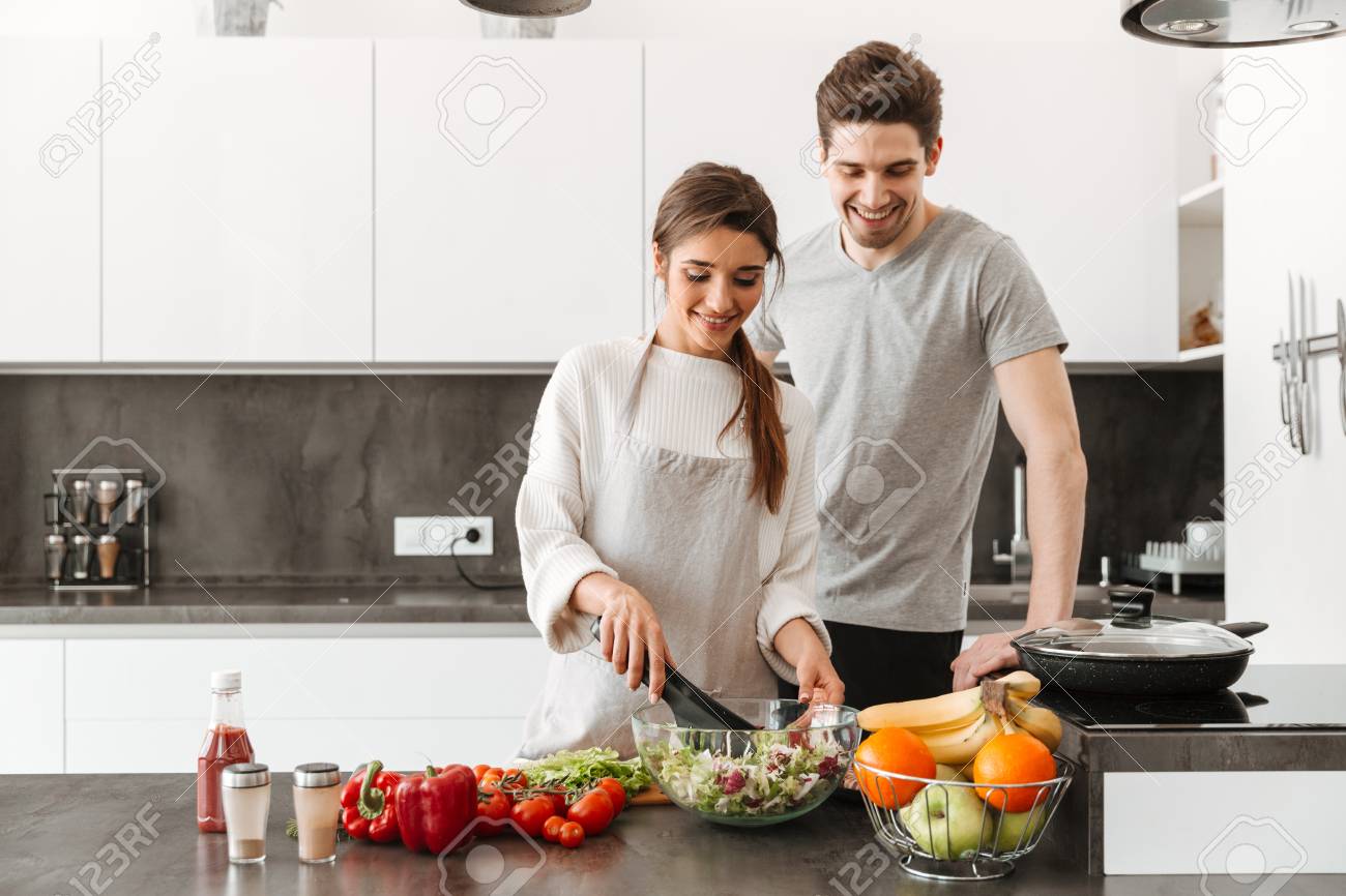 Portrait of a cheerful young couple cooking together at the kitchen - 103447931 Portrait of a cheerful young couple cooking together at the kitchen - 103447931