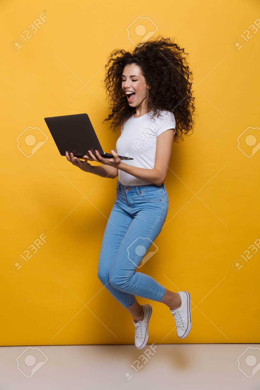 Full length photo of funny woman 20s wearing casual clothes smiling and jumping while holding black laptop isolated over yellow background - 110960851 Full length photo of funny woman 20s wearing casual clothes smiling and jumping while holding black laptop isolated over yellow background - 110960851