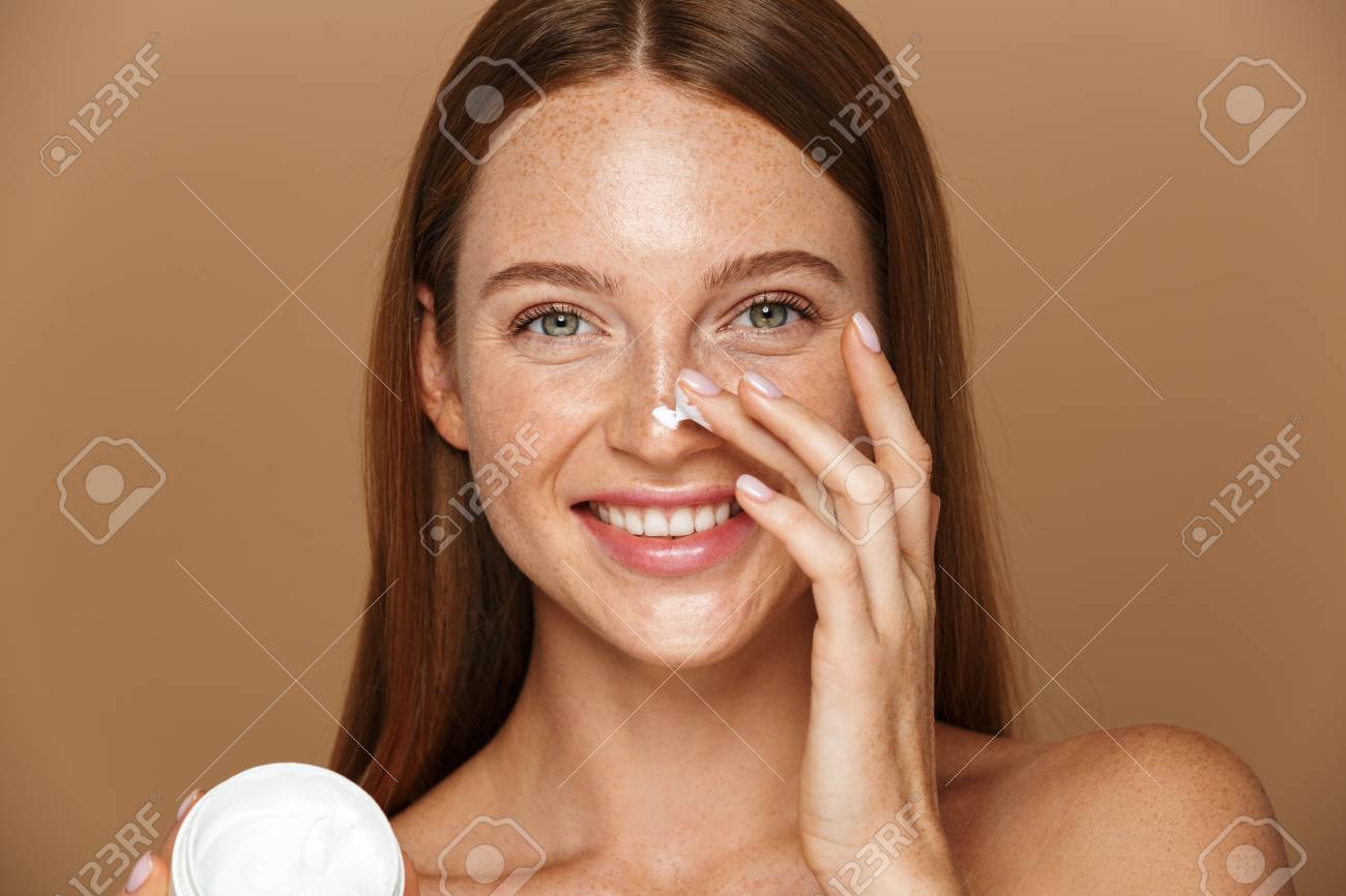 Beauty image of attractive shirtless woman smiling and holding jar with face cream isolated over beige background - 115700696 Beauty image of attractive shirtless woman smiling and holding jar with face cream isolated over beige background - 115700696
