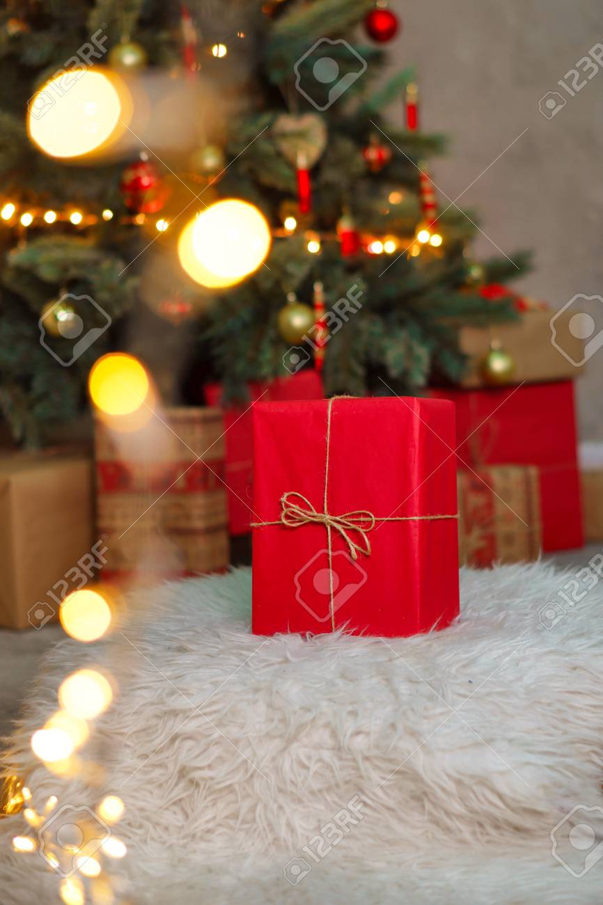 A Big Red Gift Stands Under The Christmas Tree Background For Holiday A Big Red Gift Stands Under The Christmas Tree Background For Holiday