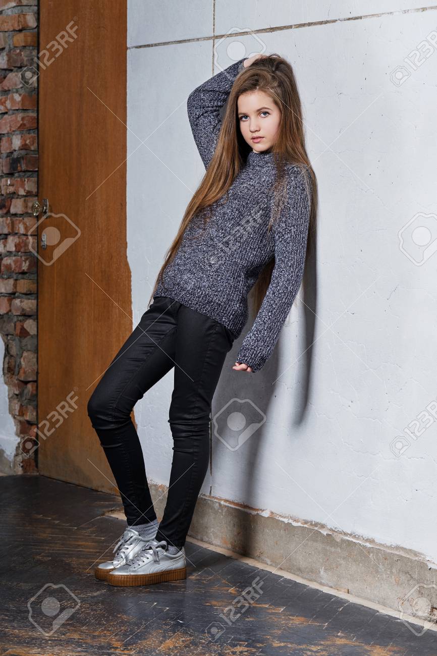 白いコンクリートの壁に寄りかかって立っているファッションティーンエイジャーの女の子 スタイリッシュな魅力的なヒップスターガール12歳 のポーズで手を上げて髪を抱えています 美しいモデルテスト 一連の写真 の写真素材 画像素材 Image