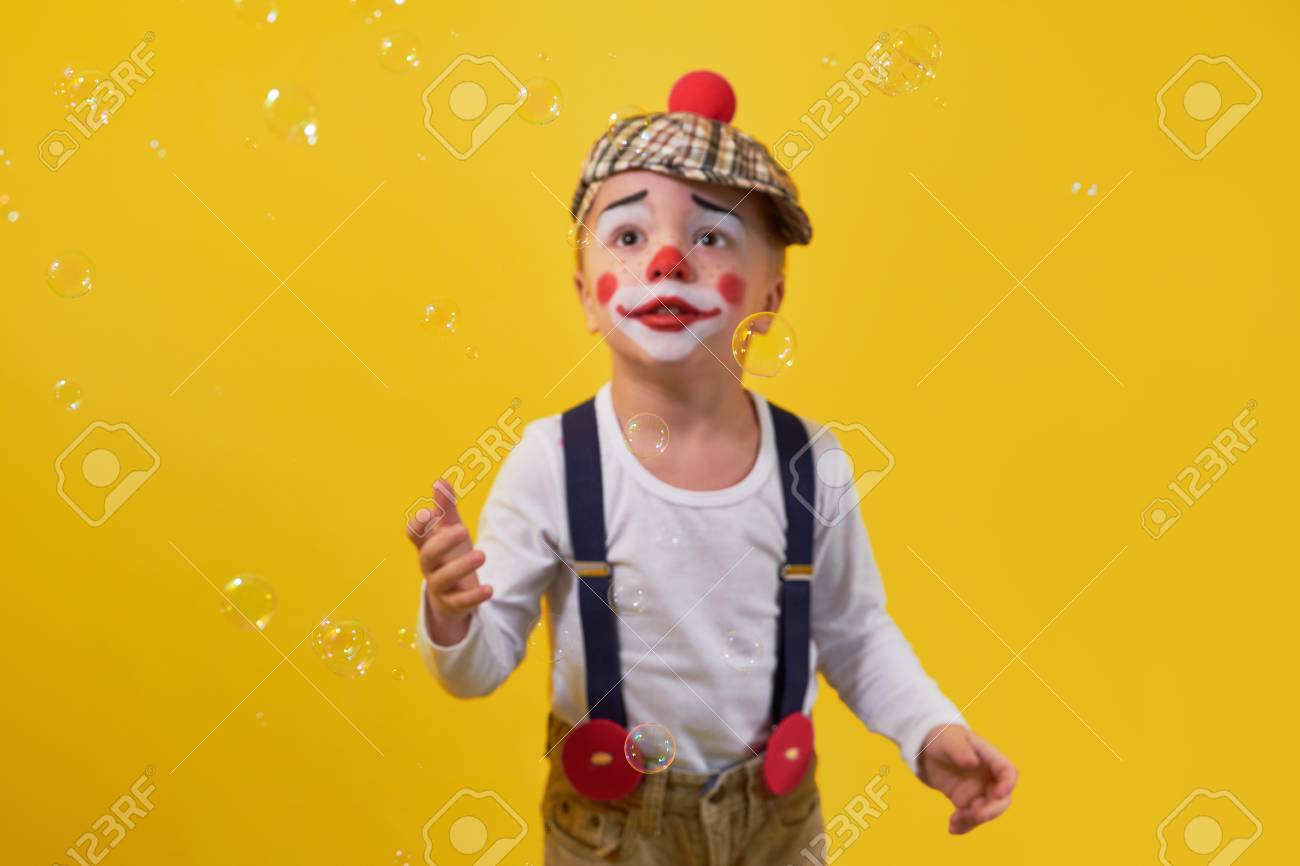 Funny Kid Clown Looking Up On Bubbles, Soft Focus.Little Boy Clown In A  Costume, Makeup,bright Yellow Background. Concept  Birthday,celebration,party.Young Kid Expression Face Calm, Curious, Sad.  Фотография, картинки, изображения и сток-фотография без ...