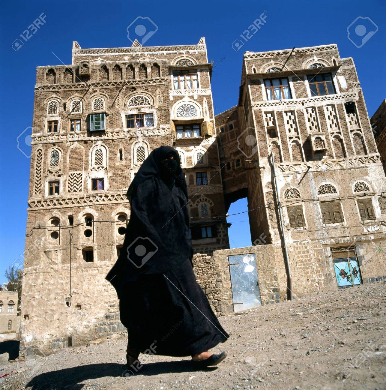 A veiled Muslim woman walks on a Sanaa street, Yemen.At background typical Yemen houses. - 6198594 A veiled Muslim woman walks on a Sanaa street, Yemen.At background typical Yemen houses. - 6198594