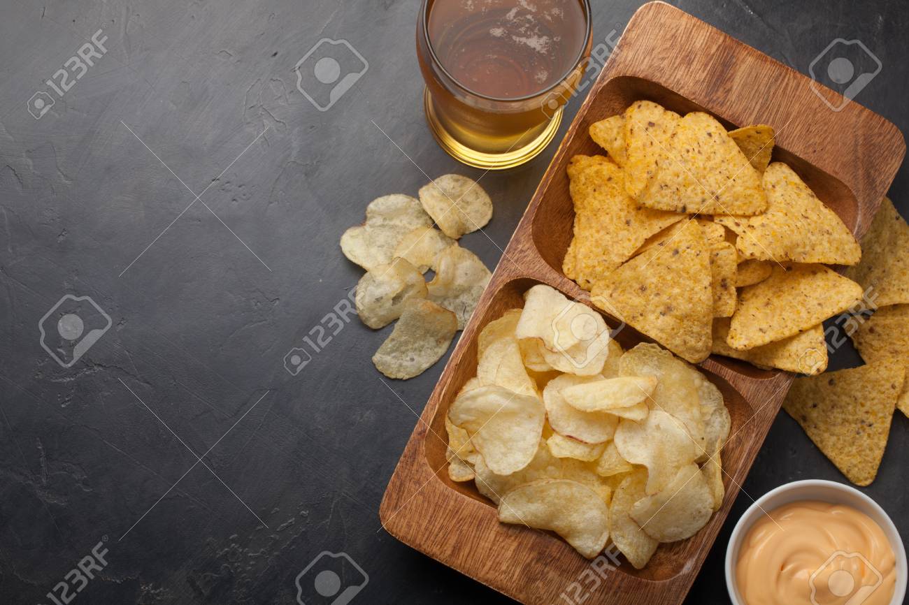 コンクリートのテーブルの上のグラスのビール ビールやスナックがチップとナチョス チーズ ソースと木製のボウルです 平面図です 領域をコピーします ドリンク スナックのサッカーの試合やパーティーのため の写真素材 画像素材 Image