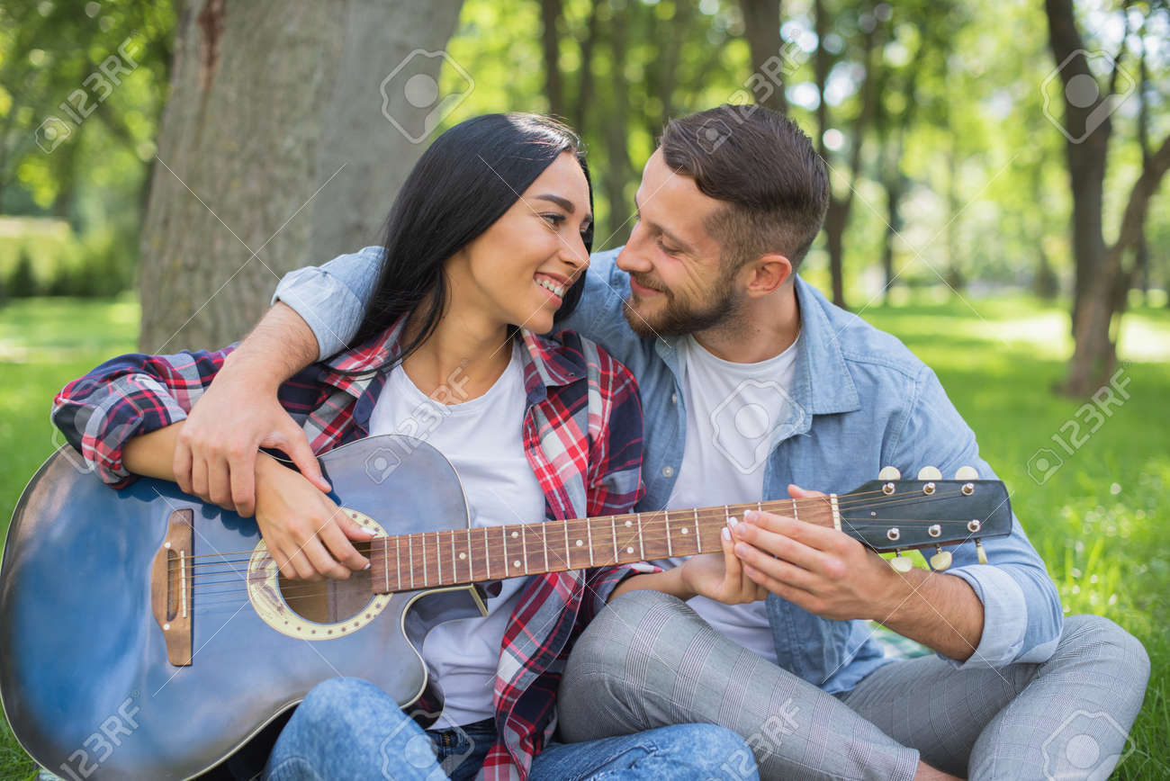 Un Hombre Guapo Enseñando A Una Chica A Tocar La Guitarra. Profesor De Guitarra Cita Romántica En La Naturaleza Con Una Guitarra. Primera Cita Perfecta Fotos, Retratos, Imágenes Y Fotografía De Archivo Un Hombre Guapo Enseñando A Una Chica A Tocar La Guitarra. Profesor De Guitarra Cita Romántica En La Naturaleza Con Una Guitarra. Primera Cita Perfecta Fotos, Retratos, Imágenes Y Fotografía De Archivo