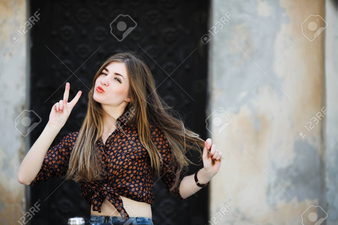 Positive girl with long hair is posing on the bicycle on the street - 122488782 Positive girl with long hair is posing on the bicycle on the street - 122488782