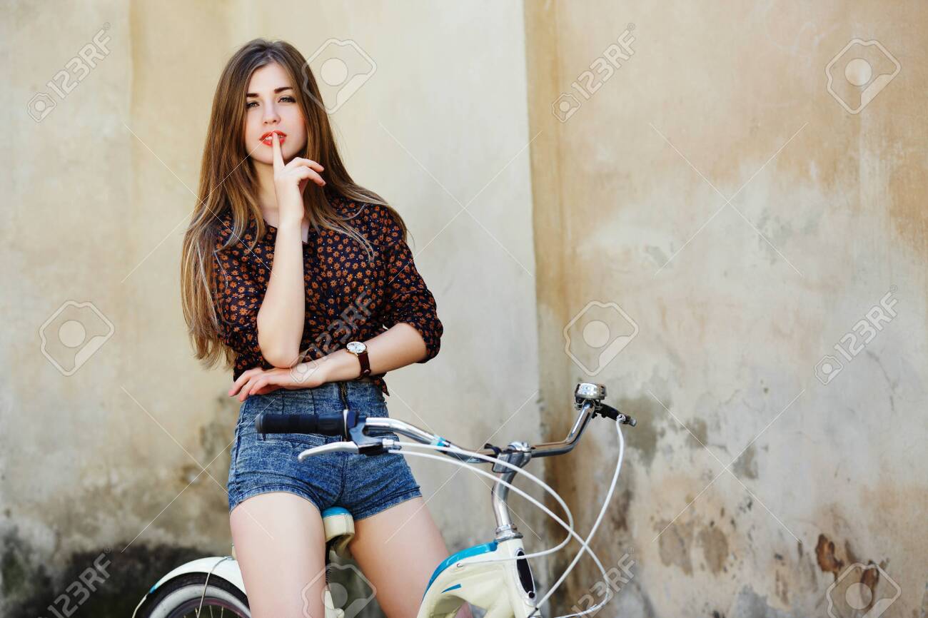 Passionate young woman with long hair is posing on the bicycle on the old wall background - 122488802 Passionate young woman with long hair is posing on the bicycle on the old wall background - 122488802