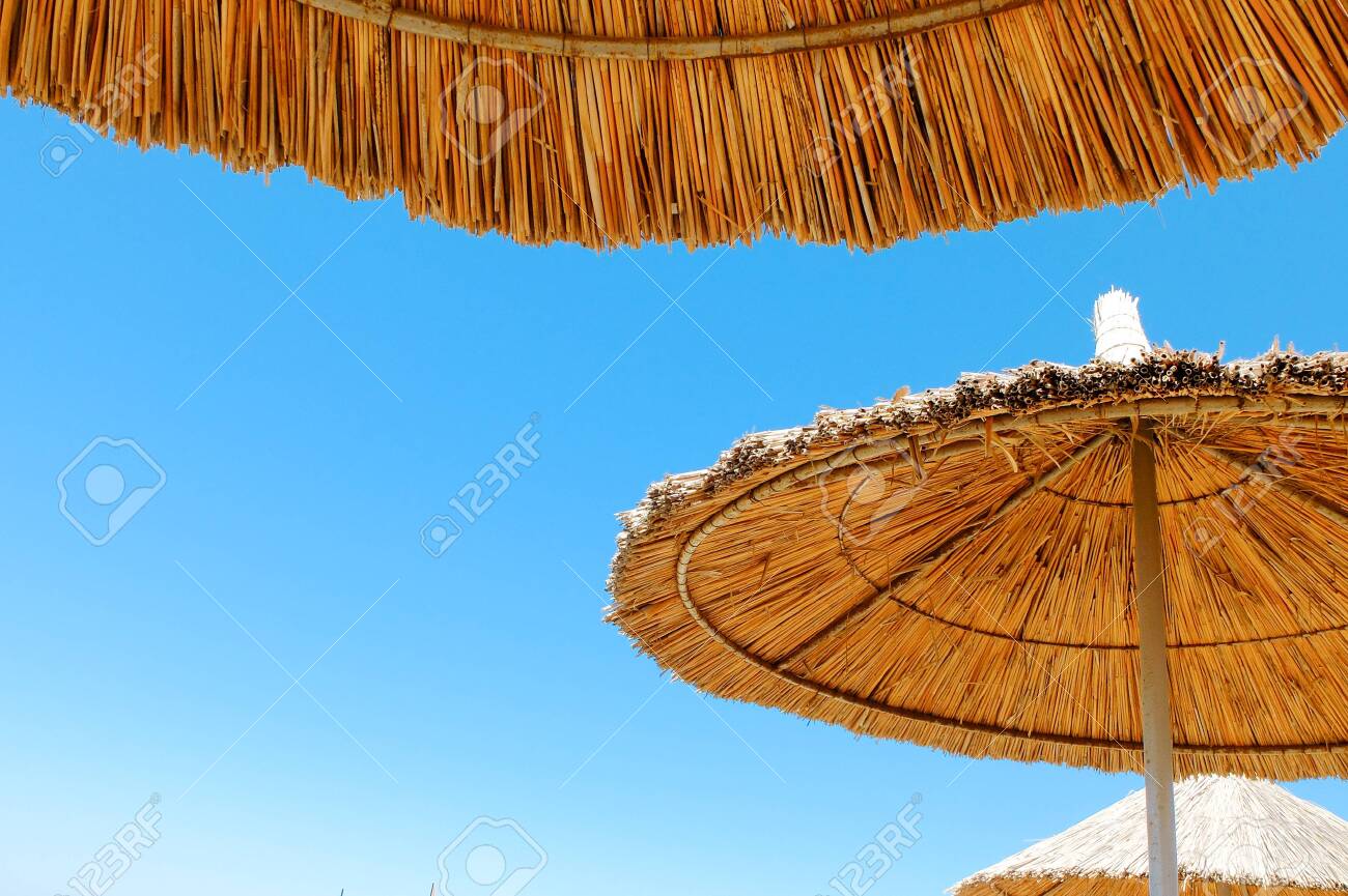 Three beach umbrellas made of straw at blue sky background - 122493986 Three beach umbrellas made of straw at blue sky background - 122493986