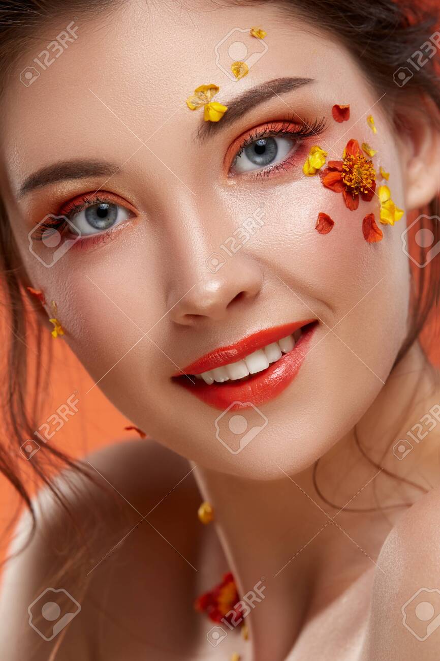 close-up portrait of pretty girl with orange make up and flowers on her face looking to the camera, fashion beauty - 125643758 close-up portrait of pretty girl with orange make up and flowers on her face looking to the camera, fashion beauty - 125643758