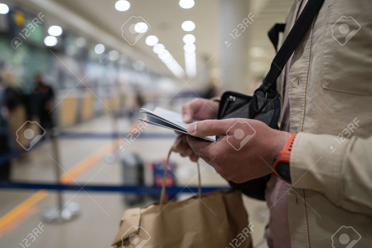Masked man use phone and keeps distance in check-in area for flight at airport in Cyprus, Paphos city, upon check-in. - 169355185 Masked man use phone and keeps distance in check-in area for flight at airport in Cyprus, Paphos city, upon check-in. - 169355185