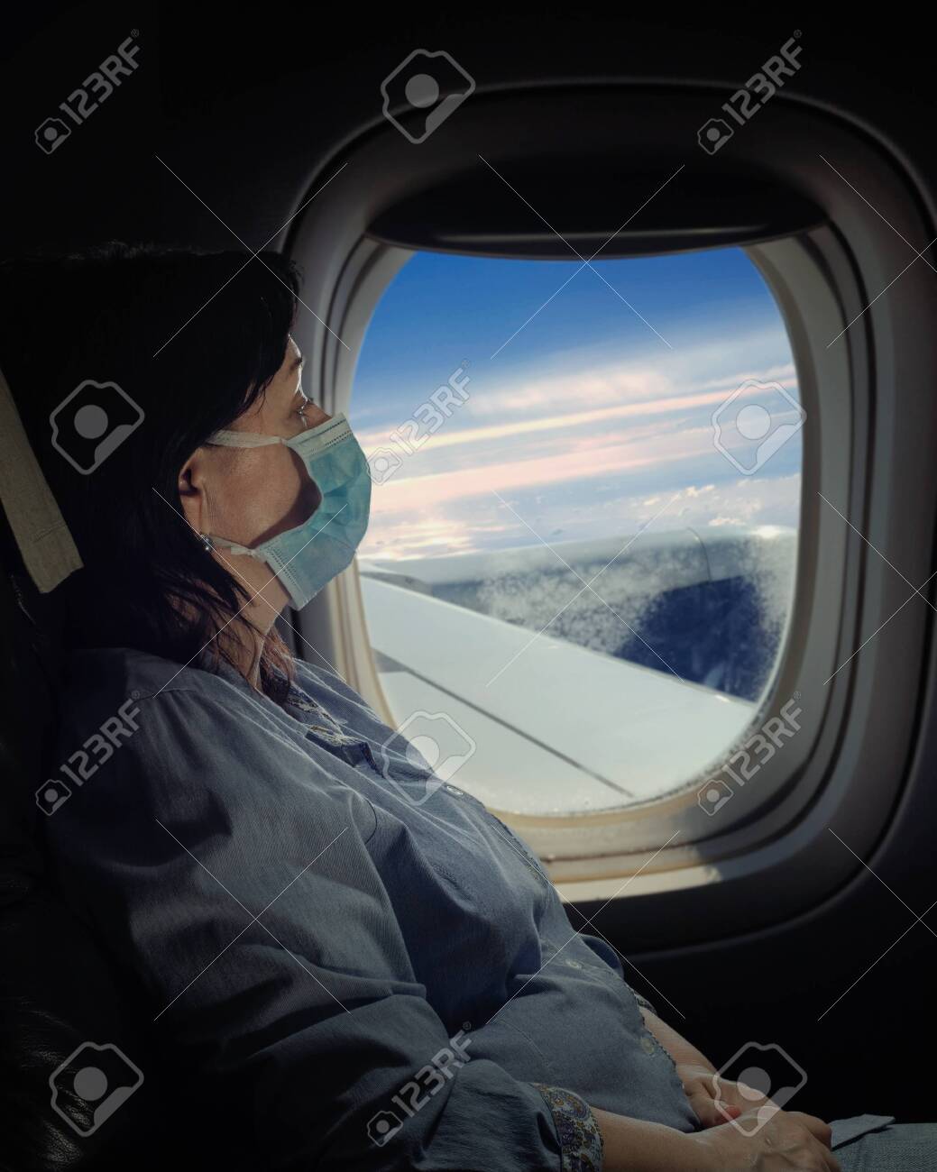 Mature Woman In Face Mask Traveling On The Airplane. Night Shot 