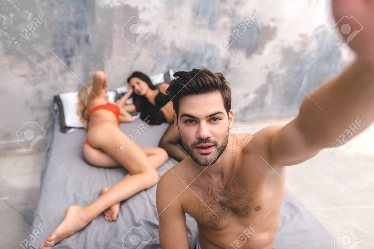 男は夜の後に目を覚ますと自分撮りを取る。男が目を覚まし、自分撮りをしながら寝室で眠っている2人の女の子。セックスパーティーのコンセプト。の写真素材・画像素材  Image 102408773