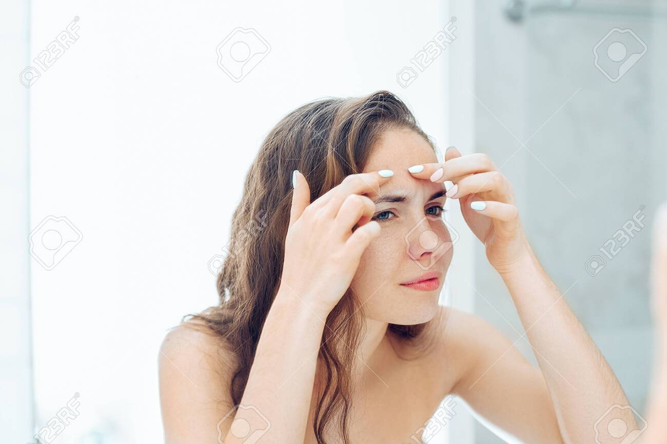 Young Woman Looking And Squeeze Acne On A Face In Front Of The Mirror. Ugly  Problem Skin Girl, Teen Girl Having Pimples. Skin Care. Beauty Фотография,  картинки, изображения и сток-фотография без роялти.