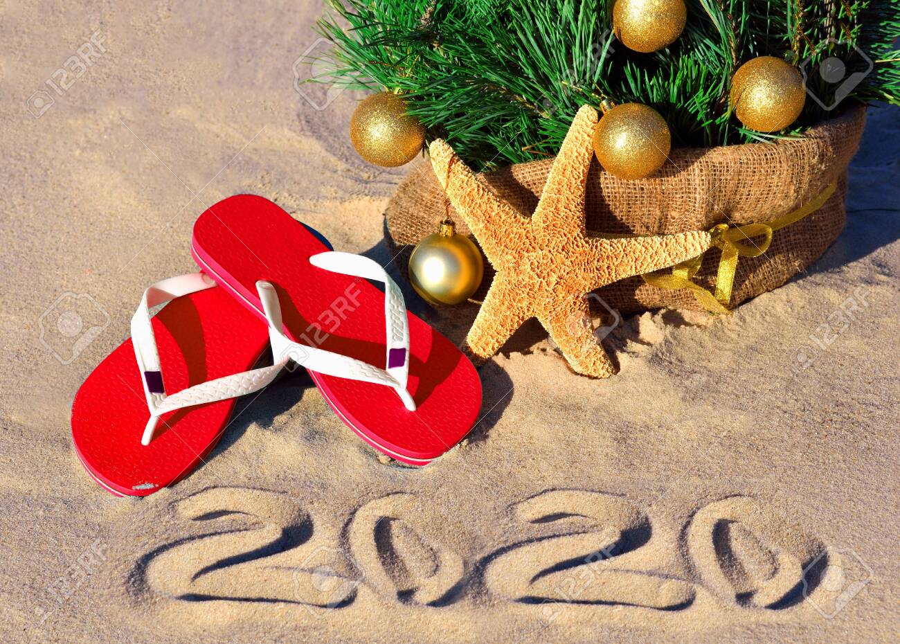 New Year 2020 on the beach. Christmas tree, starfish and slippers in sand - 137932582 New Year 2020 on the beach. Christmas tree, starfish and slippers in sand - 137932582