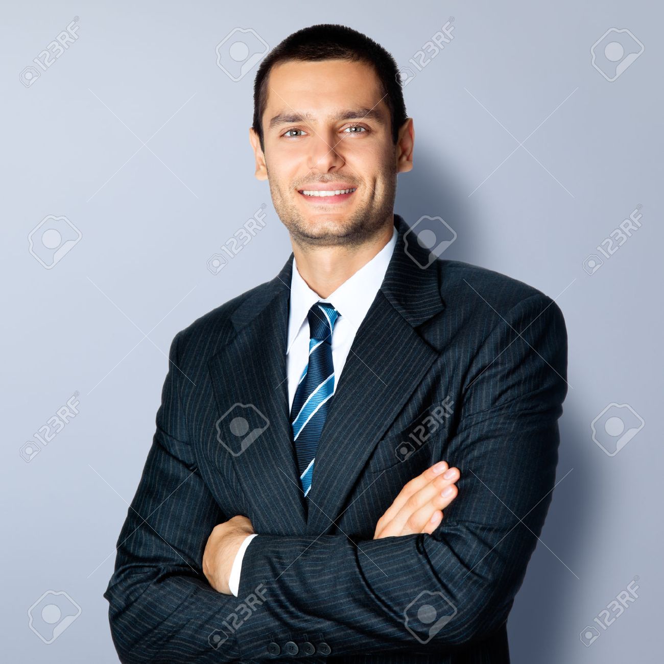 Portrait of happy smiling businessman in crossed arms pose, in black confident suit, against grey background. Caucasian male model at studio shot. Business and success concept. - 41221598 Portrait of happy smiling businessman in crossed arms pose, in black confident suit, against grey background. Caucasian male model at studio shot. Business and success concept. - 41221598