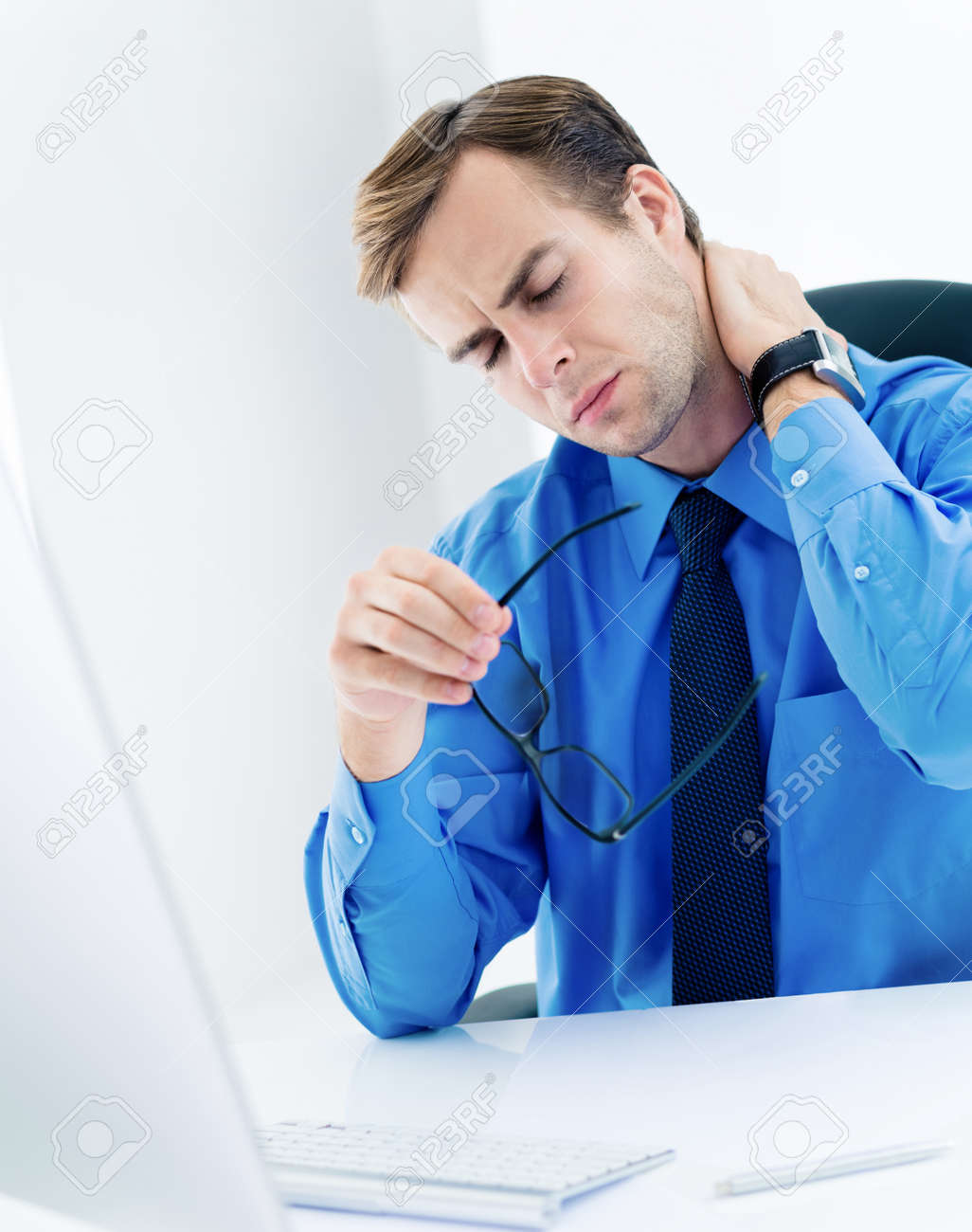 Image of frustrated, exhausted or tired business man in confident blue shirt, with glasses, touching neck. Businessman with computer at office. - 171475872 Image of frustrated, exhausted or tired business man in confident blue shirt, with glasses, touching neck. Businessman with computer at office. - 171475872