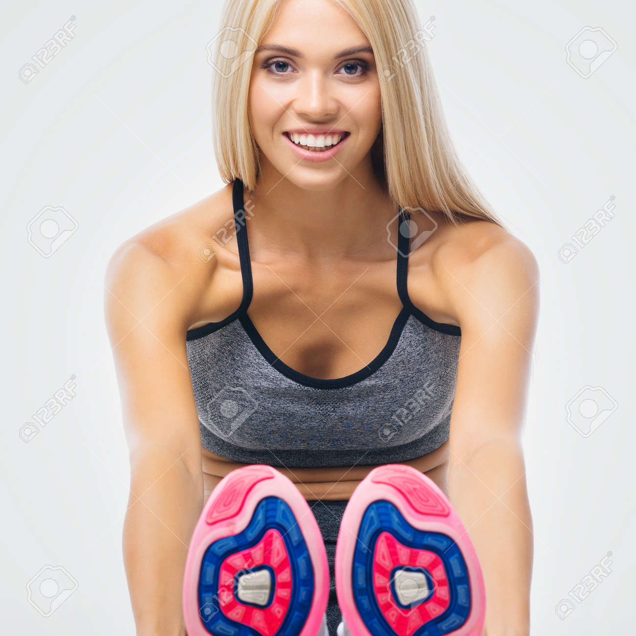 Happy smiling beautiful woman, warming up muscles before workout doing stretching exercise sitting, over grey background. Attractive blond girl in fitness studio concept. Square composition image. - 171730401 Happy smiling beautiful woman, warming up muscles before workout doing stretching exercise sitting, over grey background. Attractive blond girl in fitness studio concept. Square composition image. - 171730401