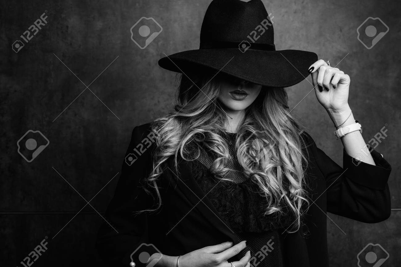 Beautiful young mysterious blond girl in black hat and black jacket on gray background. Eyes are covered with a hat. Manicure - long red nails, nail polish. Fashion, beauty. - 95004580 Beautiful young mysterious blond girl in black hat and black jacket on gray background. Eyes are covered with a hat. Manicure - long red nails, nail polish. Fashion, beauty. - 95004580