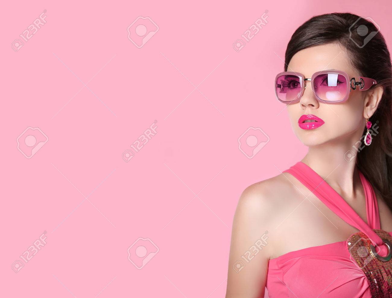 高級宝飾耳飾り長い髪 明るいメイクでサングラスの美容ファッションのモデルの女の子 グラマー女性のピンクのスタジオの背景に分離されました の写真素材 画像素材 Image