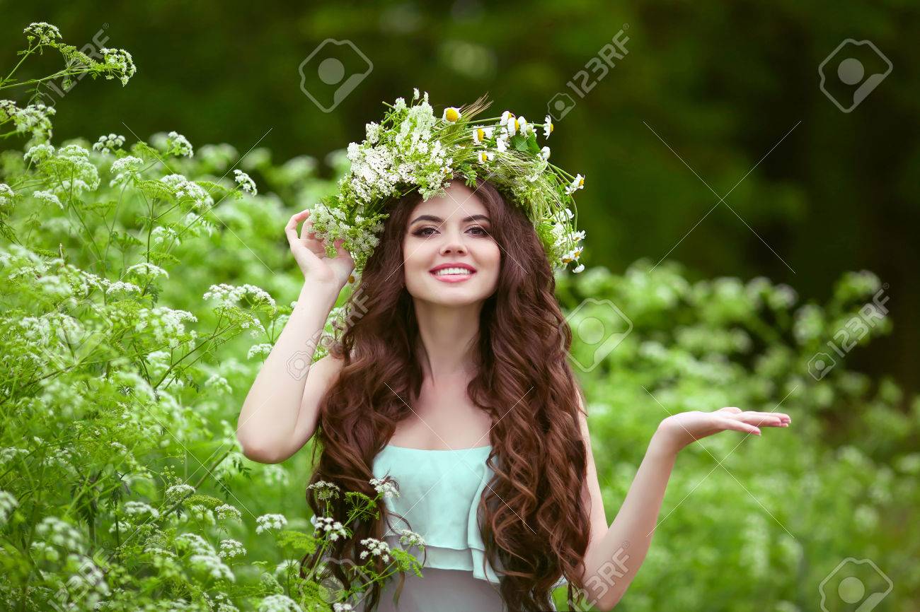 Portrait of smiling young woman in green spring park with open empty palm hand for copy space. Beautiful female with healthy long curly hair posing outdoors. - 68506470 Portrait of smiling young woman in green spring park with open empty palm hand for copy space. Beautiful female with healthy long curly hair posing outdoors. - 68506470