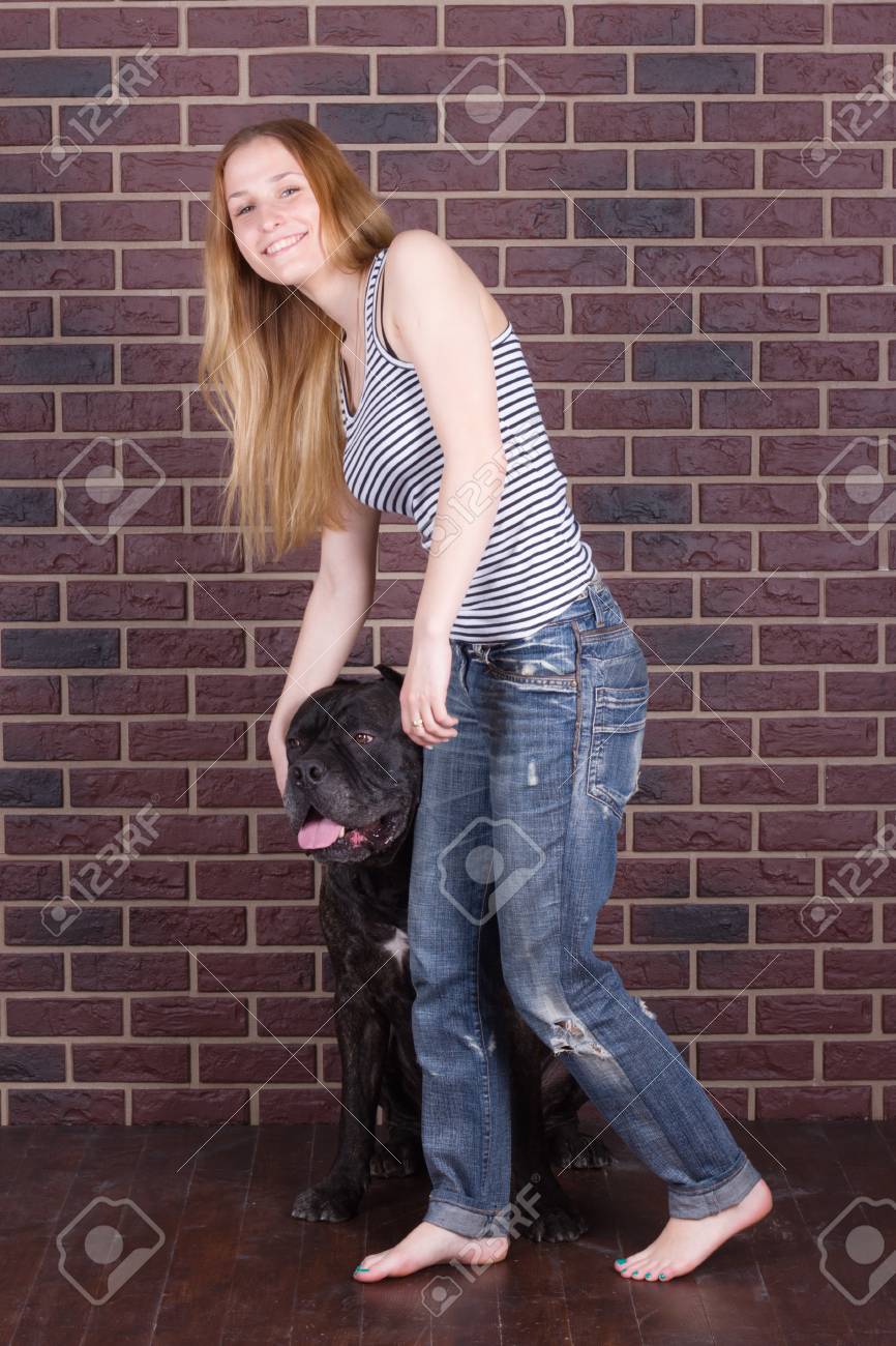 Girl In Jeans Standing Near The Wall And Hugging A Big Dog Cane