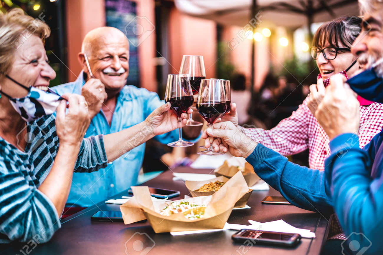 Senior people toasting wine at restaurant bar wearing open face masks - New normal life style concept with happy mature friends having fun together at garden party - Vivid filter with focus on glasses - 165216057 Senior people toasting wine at restaurant bar wearing open face masks - New normal life style concept with happy mature friends having fun together at garden party - Vivid filter with focus on glasses - 165216057