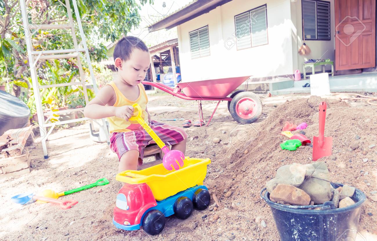 タイ赤ちゃんグッズ プラスチックのフォーク スプーン トラック ホイール手押し車が付いている砂の山の上の少年たち の写真素材 画像素材 Image