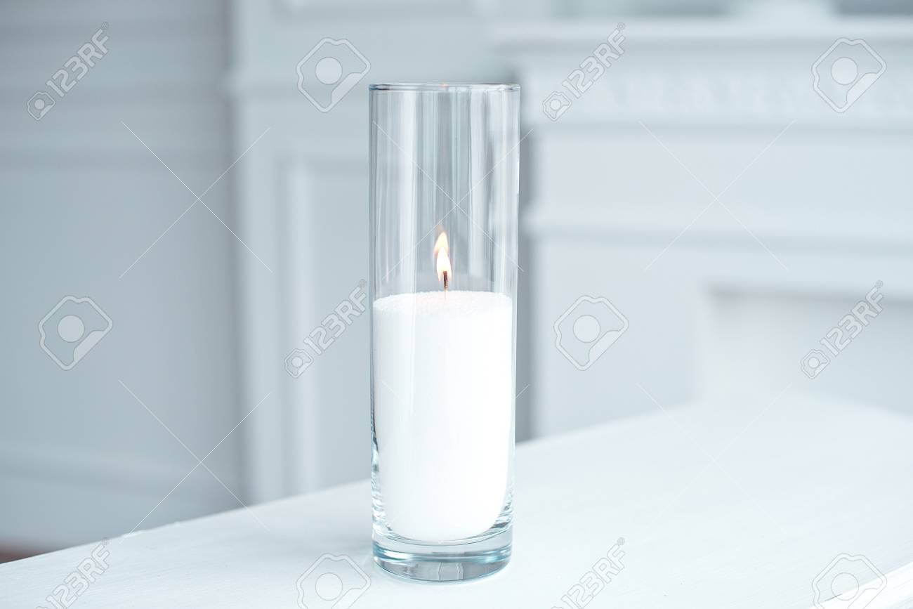 A Burning Candle In Tall Glass Vase Flask Standing On The Table