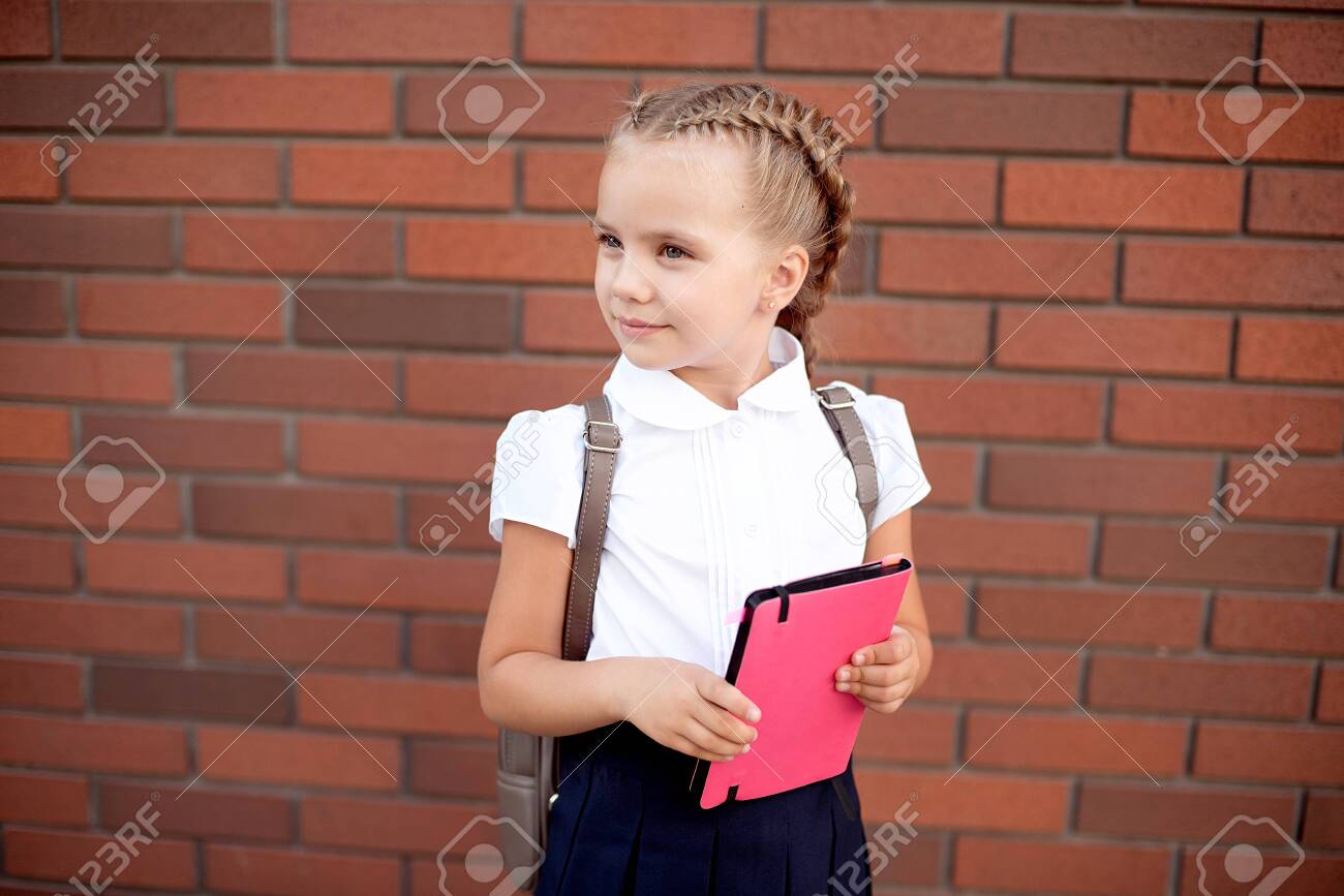 Little Girl With Blond Hair In A White Shirt And Blue Skirt Holds
