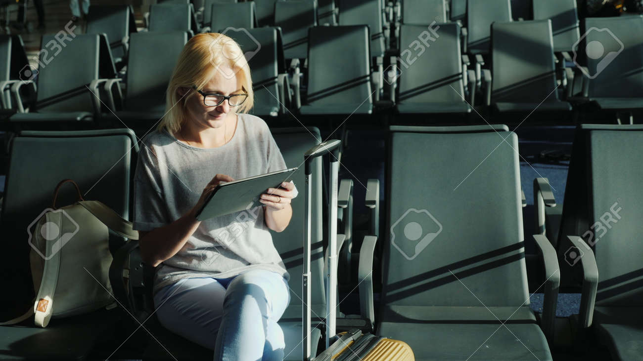 Caucasian woman is waiting for her flight. Sits in the airport terminal, uses a tablet - 167296584 Caucasian woman is waiting for her flight. Sits in the airport terminal, uses a tablet - 167296584