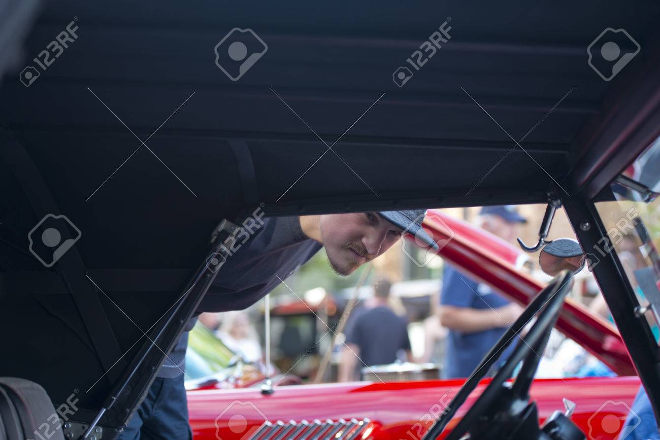 この町の休日に訪問者が多い高級ビンテージ車の都市の通りに行のディスプレイ上の展覧会で屋根を折ると元通りにされた古い珍しいレトロな赤い車 のインテリアを探しているキャップの男 の写真素材 画像素材 Image 4731
