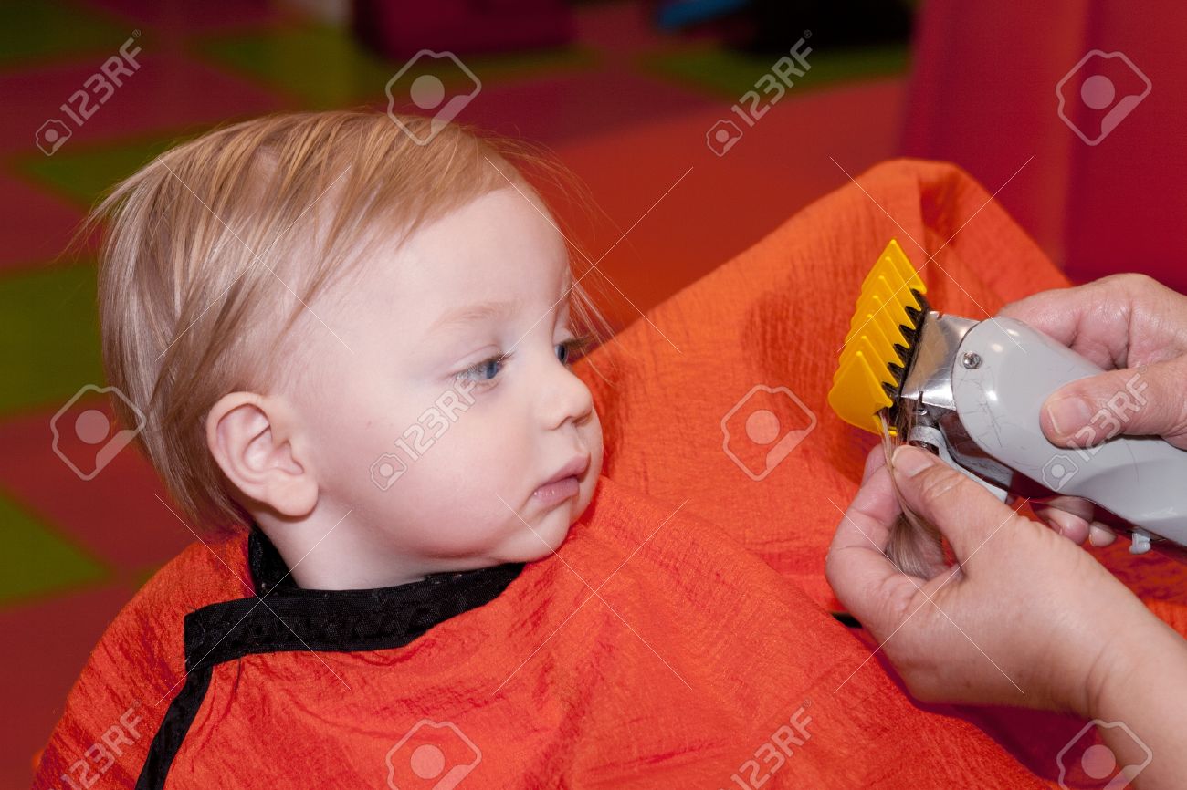 彼は理髪店での彼の最初の散髪を取得バリカンを見て男の赤ちゃん の写真素材 画像素材 Image