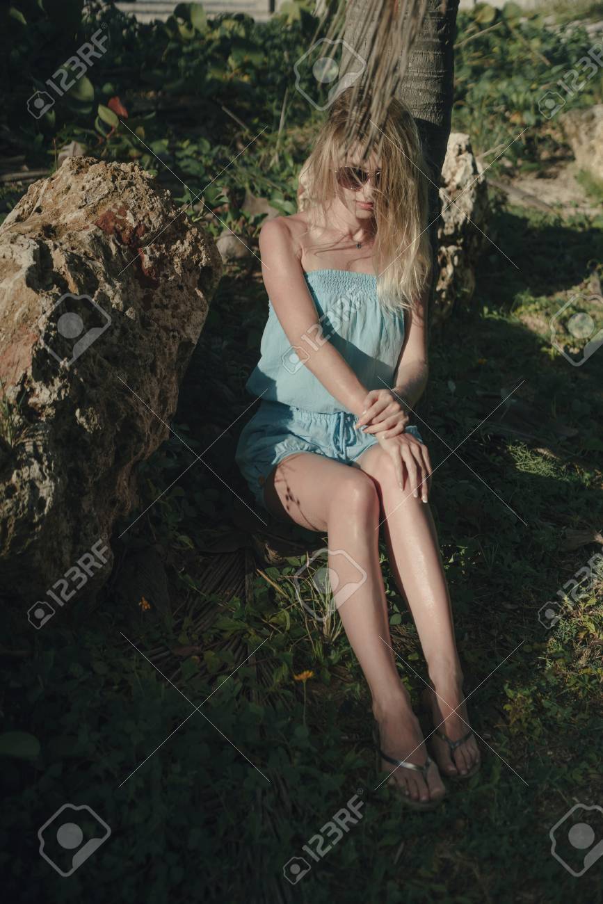 ヤシの木の木陰で座っているポーズ青いドレスで素敵な女の子 真ん中の顔と髪を風になびかせて の写真素材 画像素材 Image