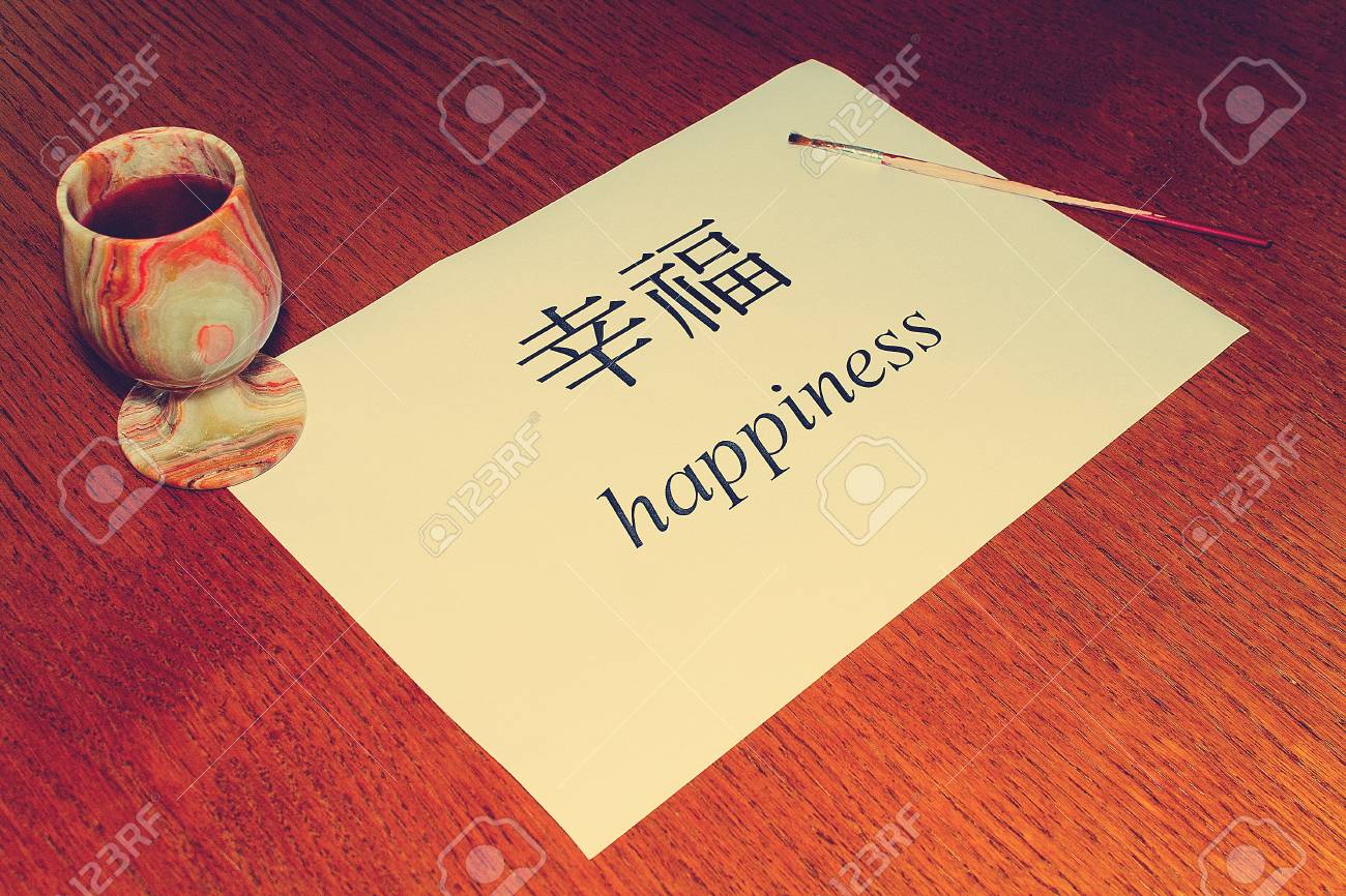 중국어의 날. 테이블 위에는 행복이라는 단어가 중국어와 영어로 쓰여진 흰 종이가 있습니다. 로열티 무료 사진, 그림, 이미지 그리고  스톡포토그래피. Image 99432123