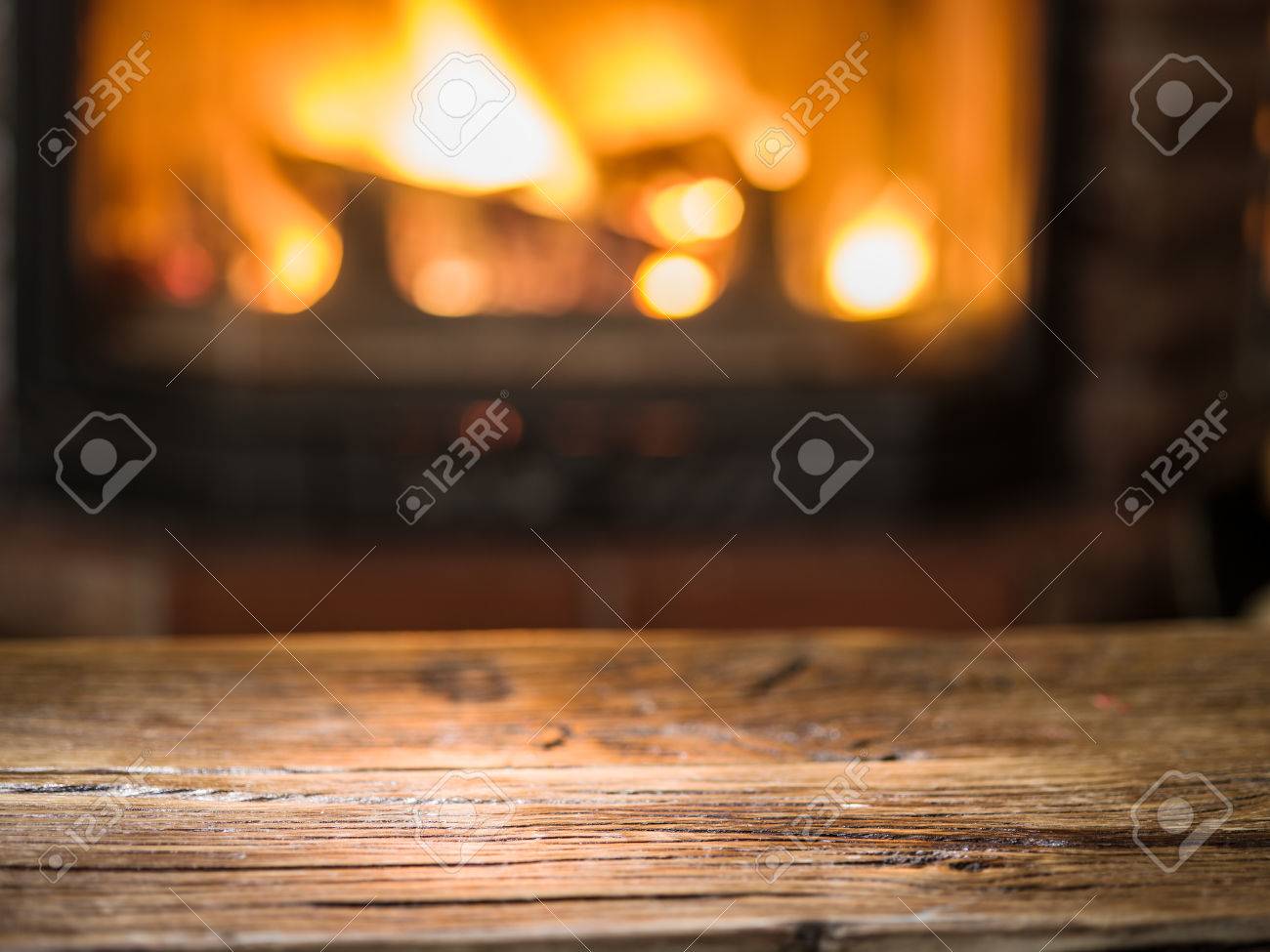 Old wooden table and fireplace with warm fire on the background. - 60157462 Old wooden table and fireplace with warm fire on the background. - 60157462