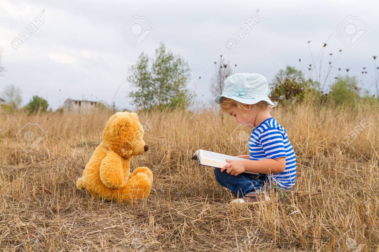 Cute girl reading book Teddy bear on the grass. - 45662441 Cute girl reading book Teddy bear on the grass. - 45662441