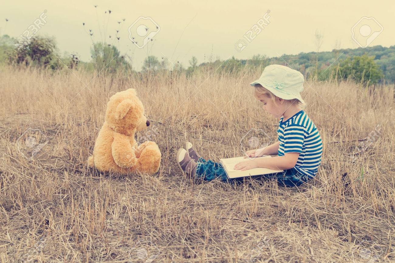Cute girl reading book Teddy bear on the grass. - 49063016 Cute girl reading book Teddy bear on the grass. - 49063016