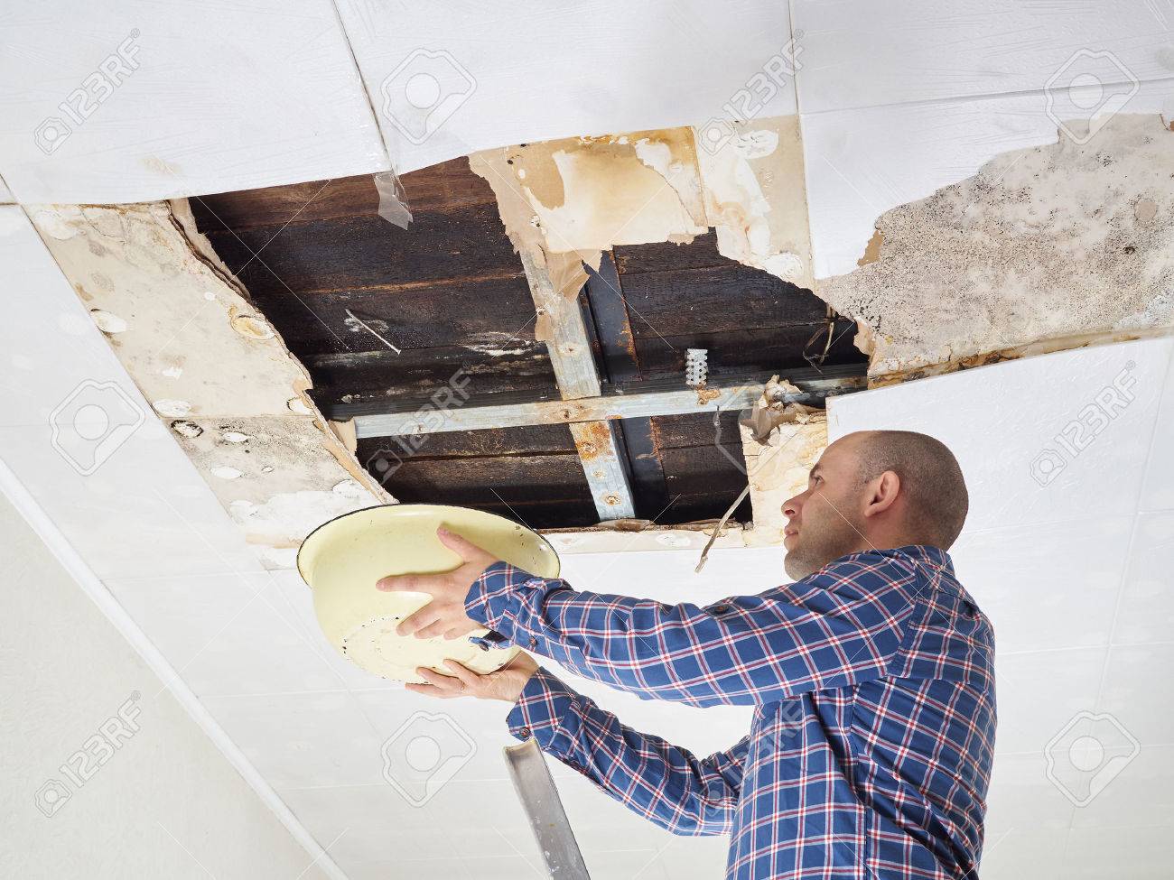 Man Collecting Water In basin From Ceiling. Ceiling panels damaged huge hole in roof from rainwater leakage.Water damaged ceiling . - 57035838 Man Collecting Water In basin From Ceiling. Ceiling panels damaged huge hole in roof from rainwater leakage.Water damaged ceiling . - 57035838