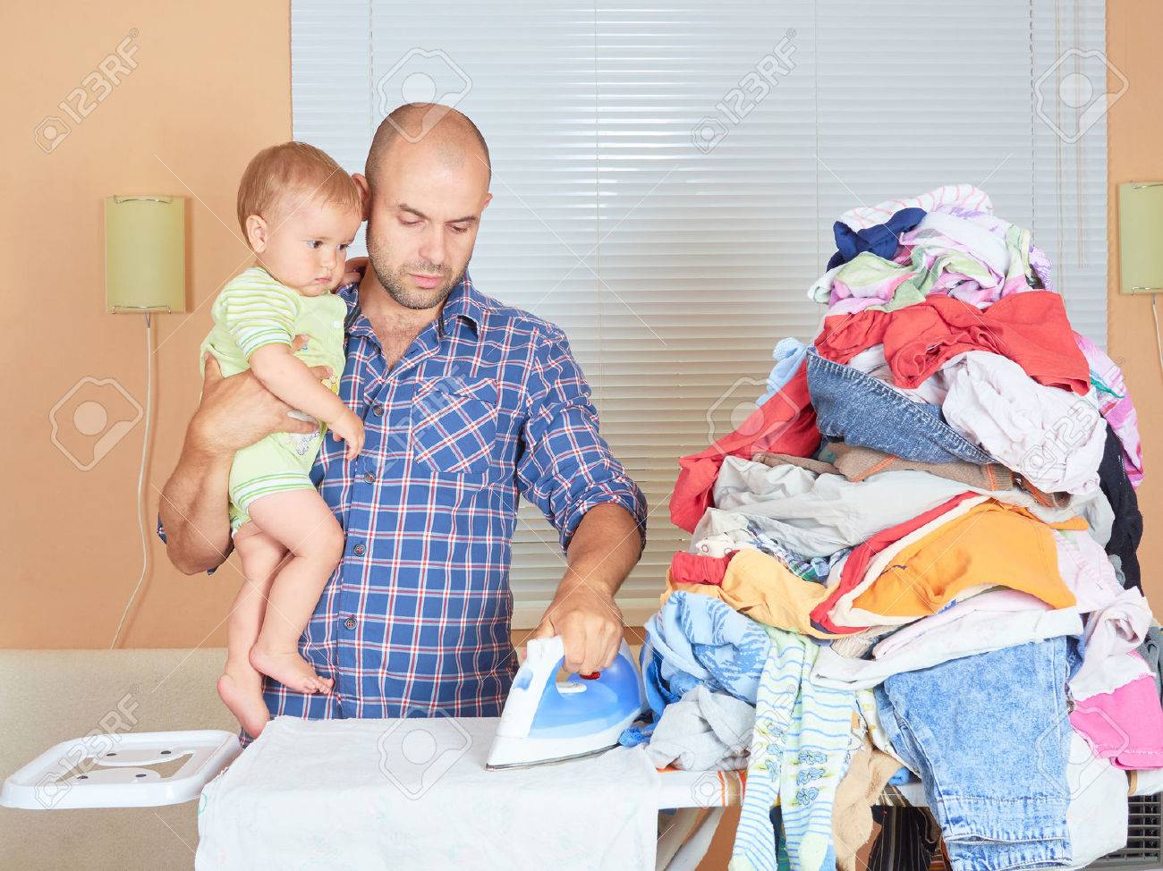 Caucasian man father and son in his hands, ironed clothes in the room near the window. Homework. - 59949789 Caucasian man father and son in his hands, ironed clothes in the room near the window. Homework. - 59949789