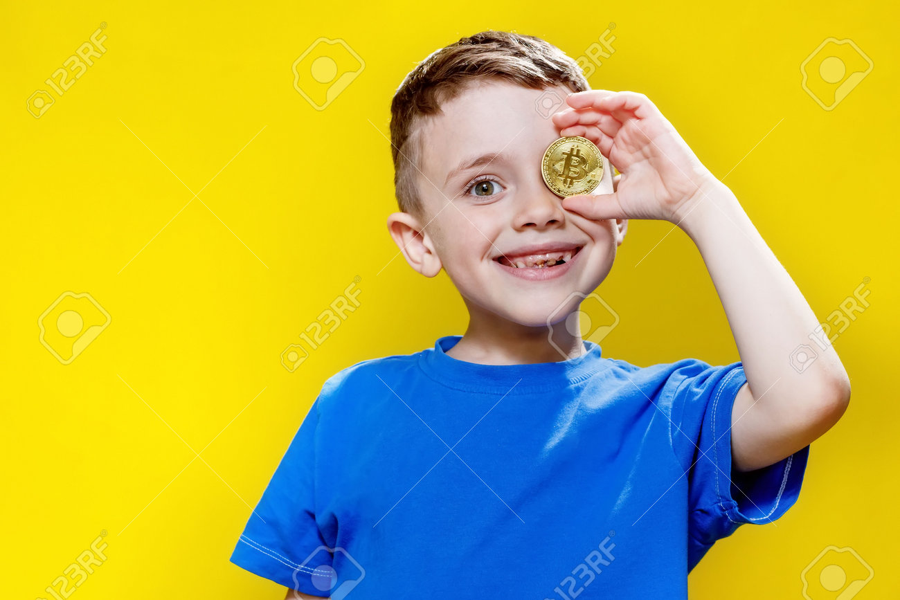 黄色い背景に目の前にビットコインを持つ青いTシャツを着た小さな幸せな就学前の男の子。の写真素材・画像素材 Image 191608613