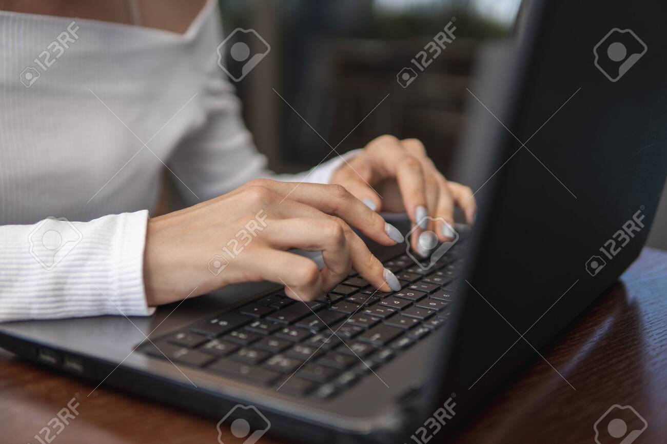 Beautiful young woman in white t-shirt is working on laptop and smiling while sitting outdoors in cafe. Young female using laptop for work. Female freelancer working on laptop in an outdoor cafe. - 137563626 Beautiful young woman in white t-shirt is working on laptop and smiling while sitting outdoors in cafe. Young female using laptop for work. Female freelancer working on laptop in an outdoor cafe. - 137563626