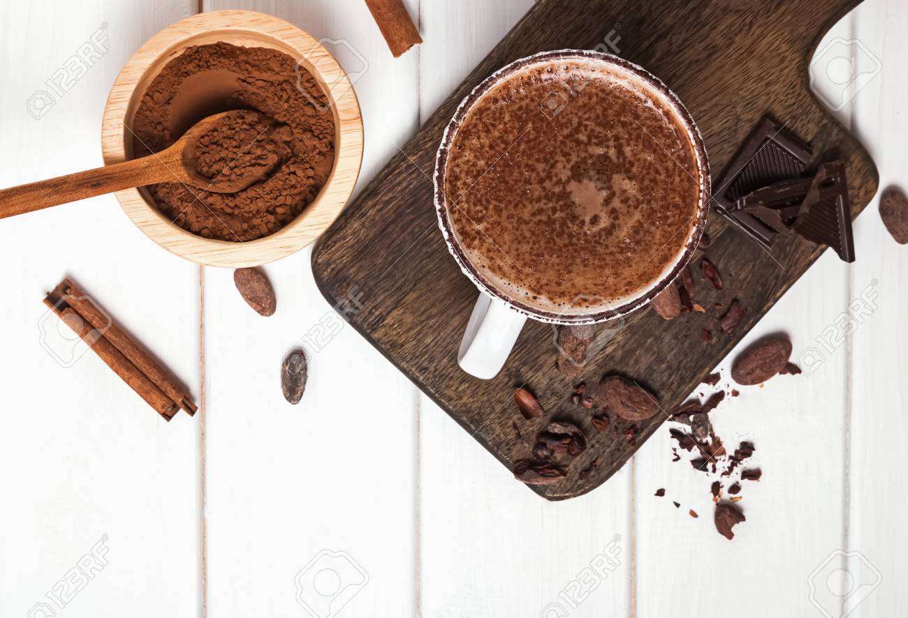 Hot chocolate in the cup, cocoa beans and powder on the white wooden table - 118170615 Hot chocolate in the cup, cocoa beans and powder on the white wooden table - 118170615