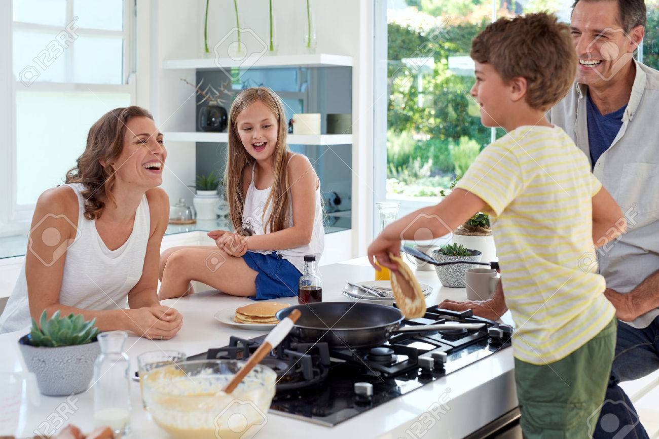 Happy caucasian family standing around stove, son making pancakes on stove - 49223934 Happy caucasian family standing around stove, son making pancakes on stove - 49223934