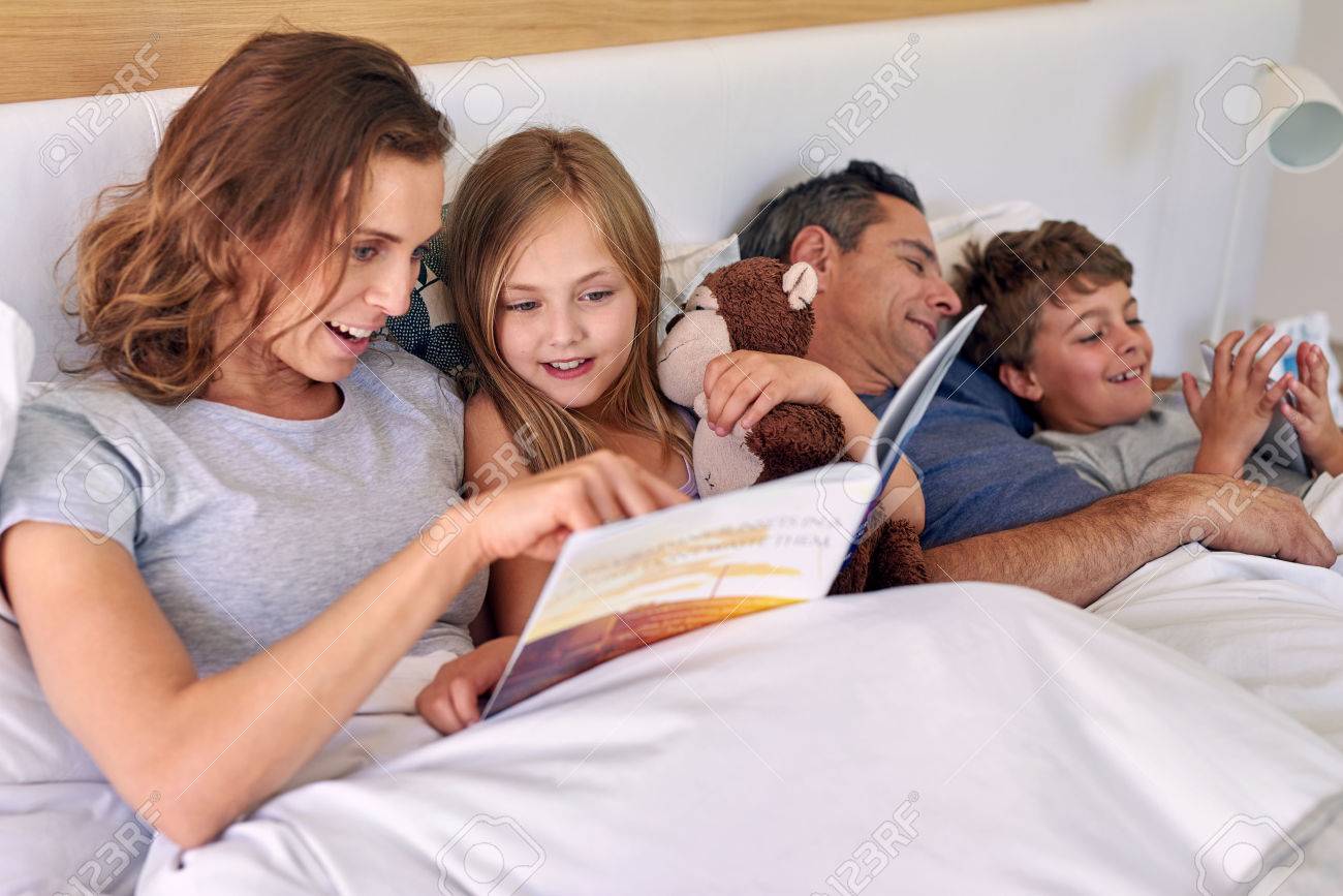 caucasian family laying in bed, mother and daughter reading father and son playing games on tablet device - 49228351 caucasian family laying in bed, mother and daughter reading father and son playing games on tablet device - 49228351