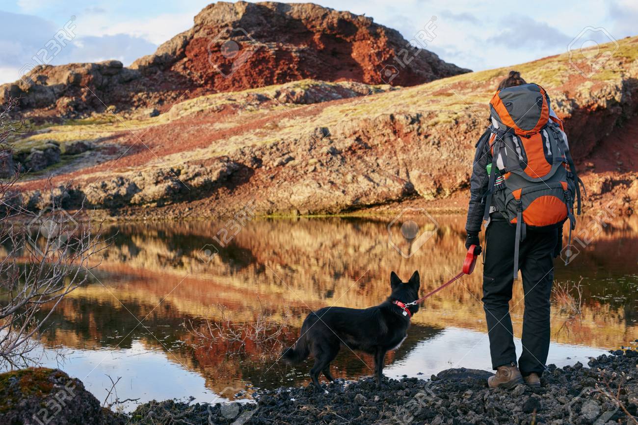 Woman with backpack and pet dog looking over the scenic lake and enjoying the view after a hard hike - 54381061 Woman with backpack and pet dog looking over the scenic lake and enjoying the view after a hard hike - 54381061