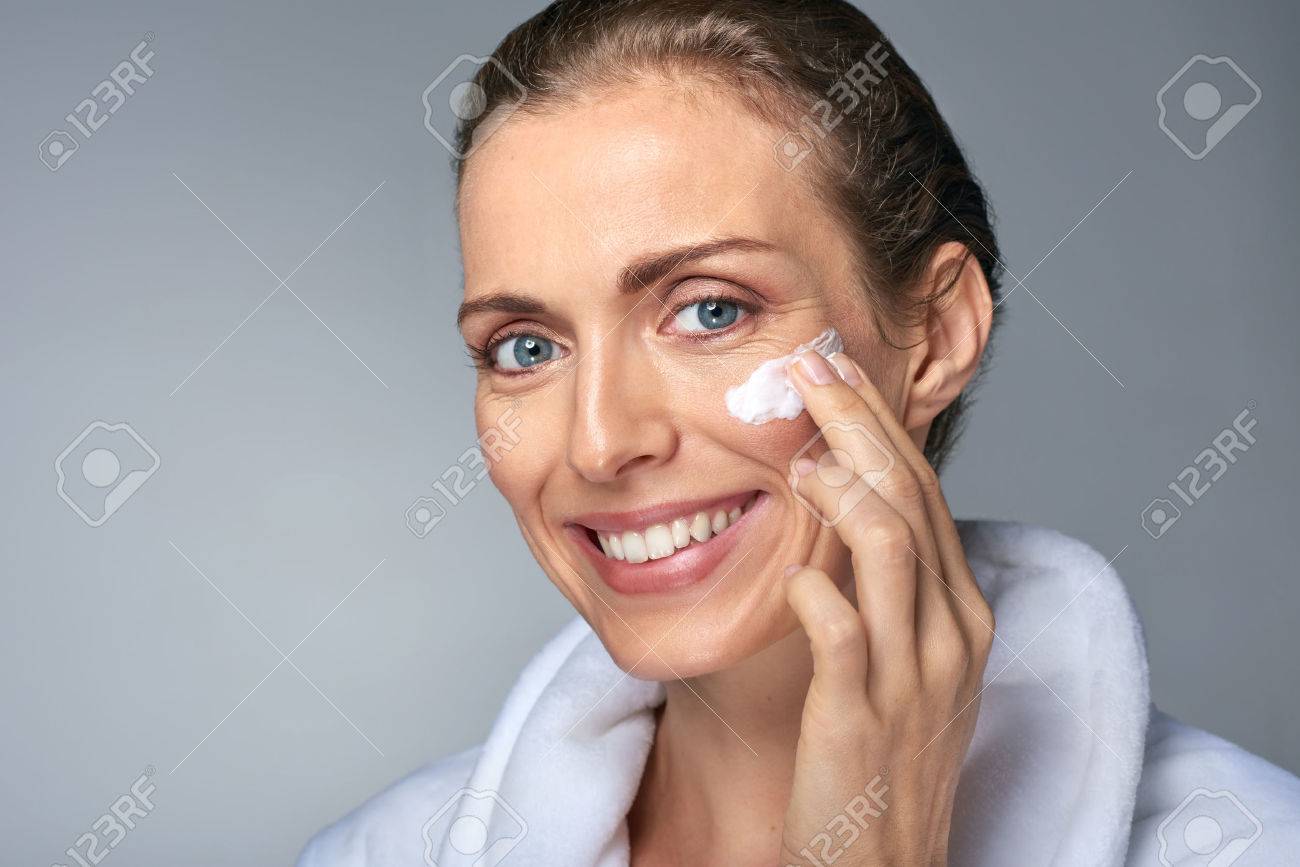 portrait of beautiful radiant mature woman applying some cream to her face, skin care cosmetics wellness concept - 56782540 portrait of beautiful radiant mature woman applying some cream to her face, skin care cosmetics wellness concept - 56782540